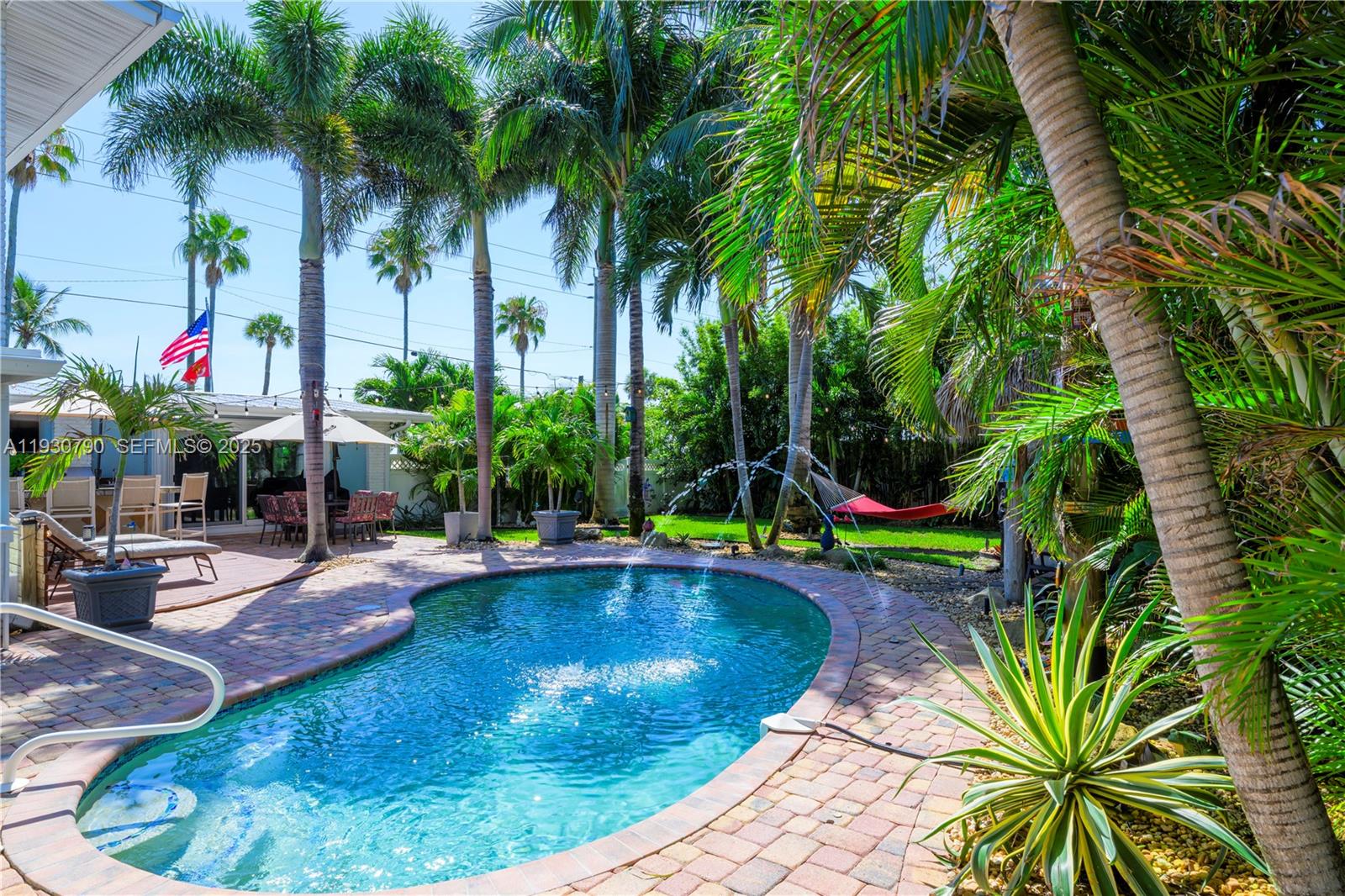 A backyard features a kidney-shaped swimming pool with fountains, a brick patio, and palm trees — 13549 S Indian River Dr, Jensen Beach FL 34957, JENSEN BEACH, FL