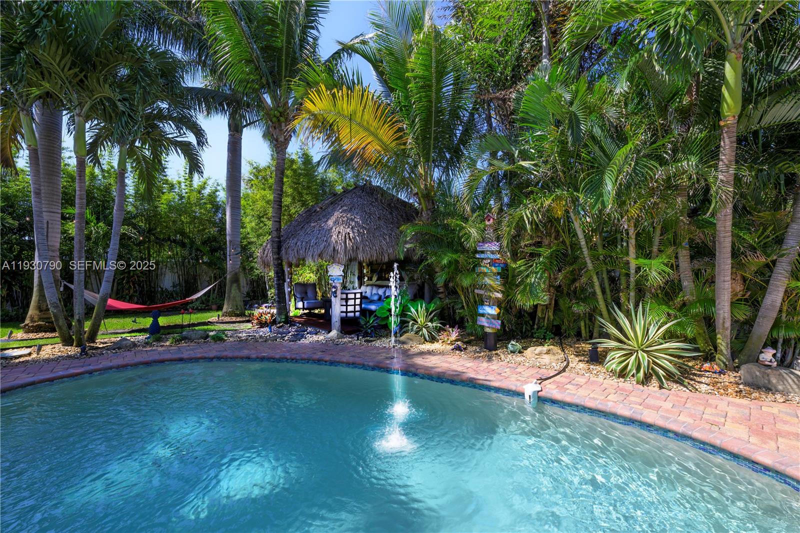A backyard swimming pool features a fountain, a tiki hut, and lush tropical landscaping — 13549 S Indian River Dr, Jensen Beach FL 34957, JENSEN BEACH, FL