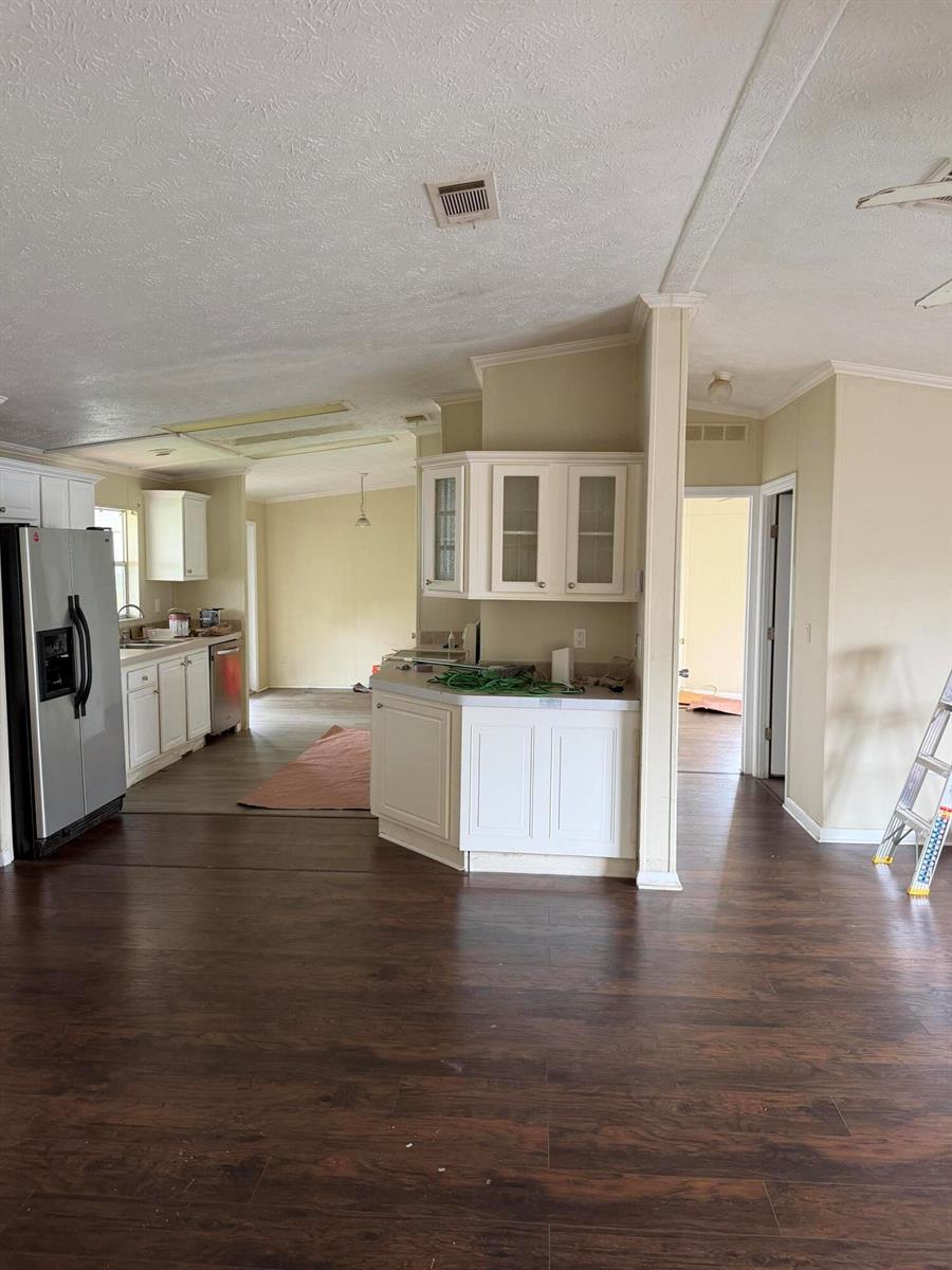 An open-concept kitchen and living area with white cabinets, dark wood flooring, and beige walls — 8557 SW 18th Street, Davie FL 33324, DAVIE, FL