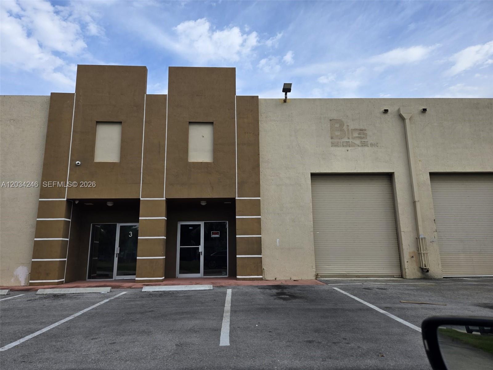 A commercial building exterior features two brown entrance bays and two large roll-up warehouse doors — HIALEAH GARDENS, FL