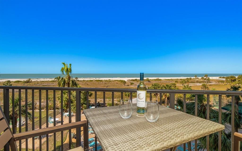 A balcony with a wicker table, wine bottle, and glasses overlooking a beach and ocean — 1230 GULF BOULEVARD UNIT 402, CLEARWATER BEACH, FL