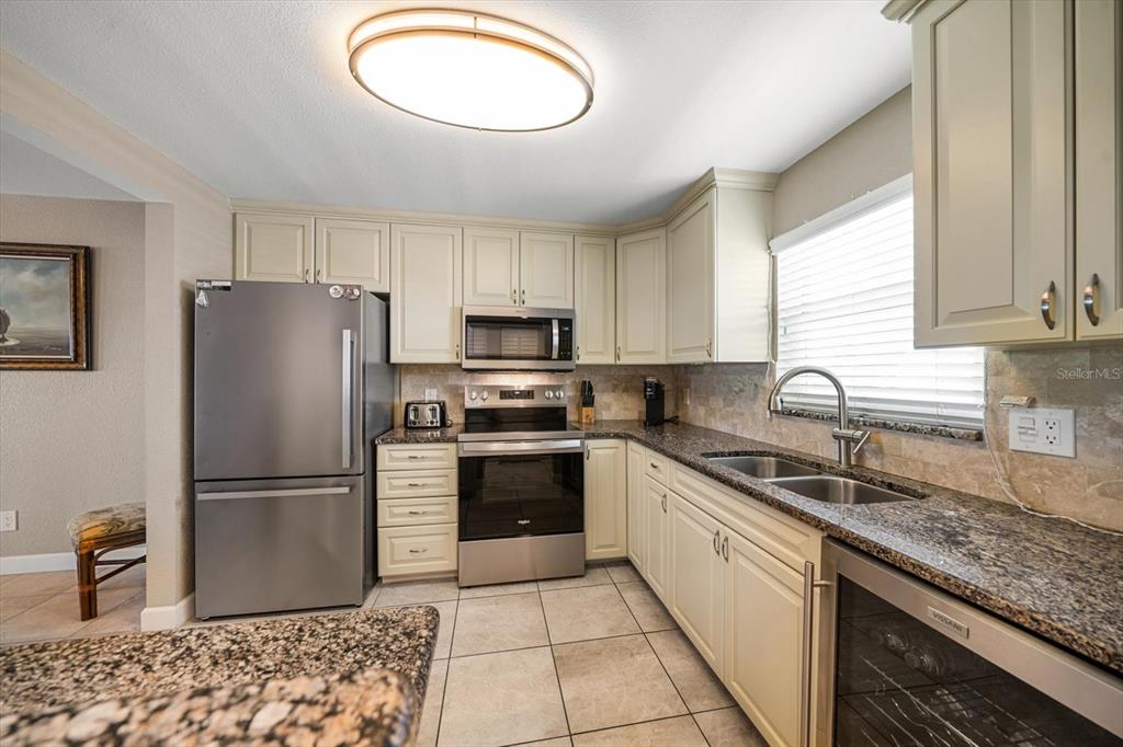A kitchen features stainless steel appliances, granite countertops, cream-colored cabinets, and light-colored tile flooring — 1230 GULF BOULEVARD UNIT 402, CLEARWATER BEACH, FL