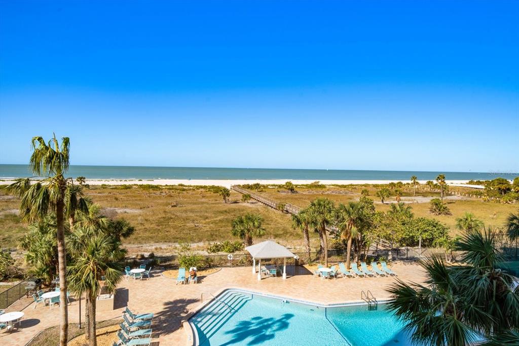 An elevated view of a swimming pool, palm trees, and a boardwalk leading to the beach — 1230 GULF BOULEVARD UNIT 402, CLEARWATER BEACH, FL