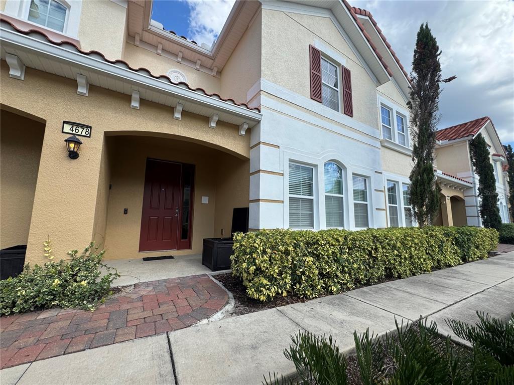 A two-story townhouse exterior features a red front door, brick walkway, and manicured hedges — 4678 TERRASONESTA DRIVE, DAVENPORT, FL