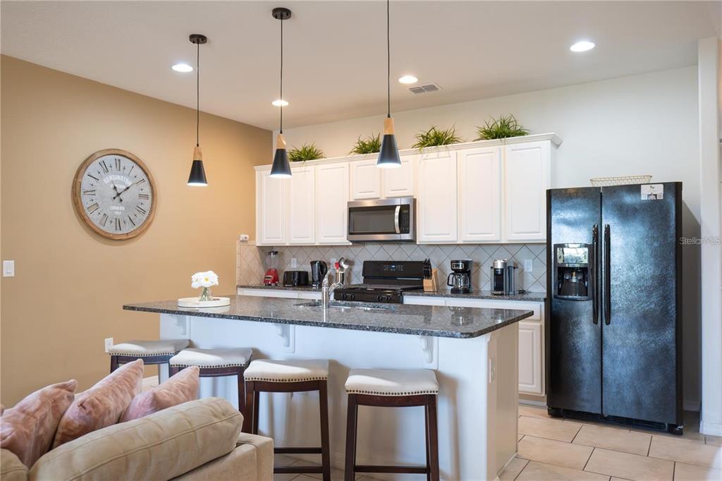 A kitchen features white cabinets, granite countertops, a black refrigerator, and a breakfast bar island — 4678 TERRASONESTA DRIVE, DAVENPORT, FL