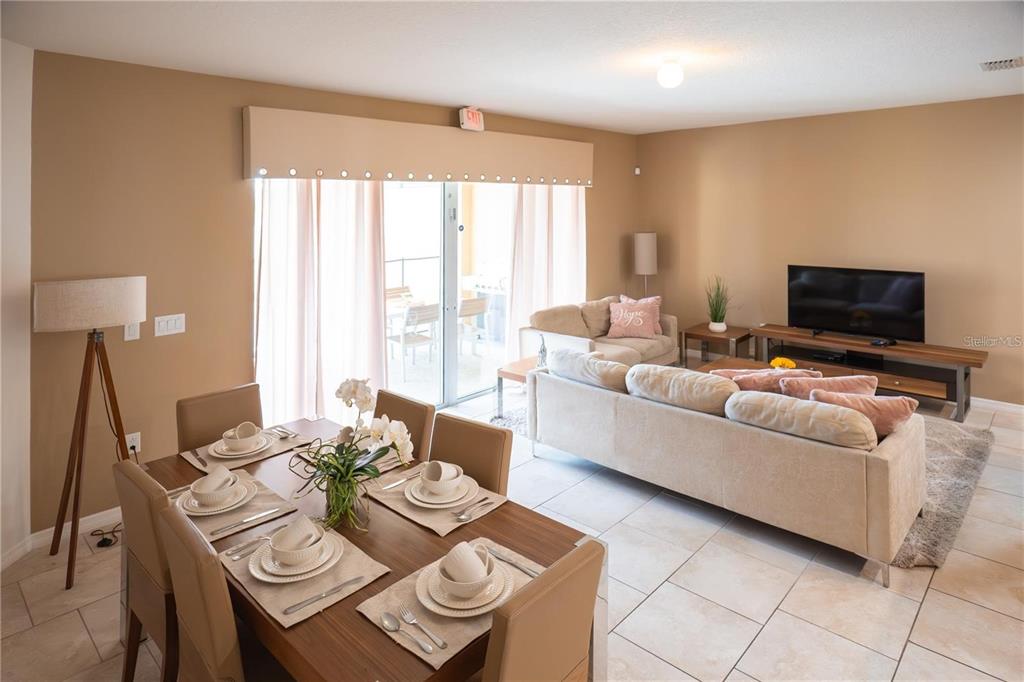 An open-concept living and dining area features tile flooring, neutral walls, and a sliding glass door — 4678 TERRASONESTA DRIVE, DAVENPORT, FL