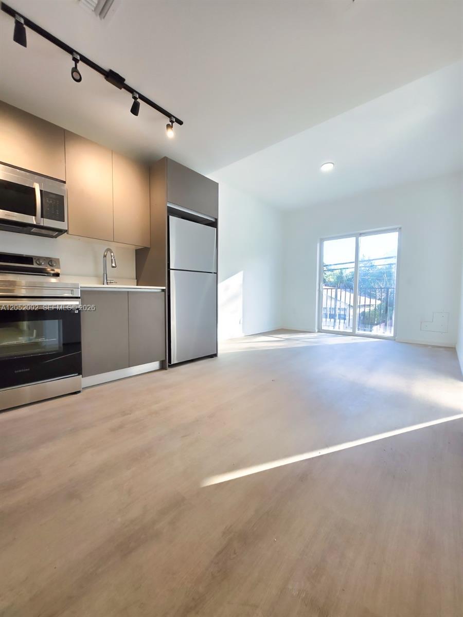 A modern kitchen with stainless steel appliances and light wood flooring opens to a balcony — 8106 NE 1st Ave # 13, Miami FL 33138, MIAMI, FL