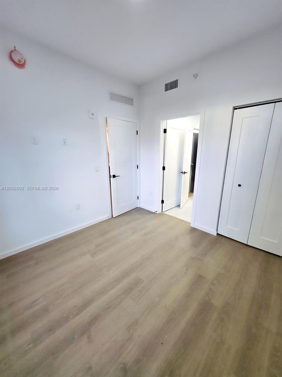 A bedroom features light wood-look flooring, white walls, two doors, and a closet — 8106 NE 1st Ave # 13, Miami FL 33138, MIAMI, FL