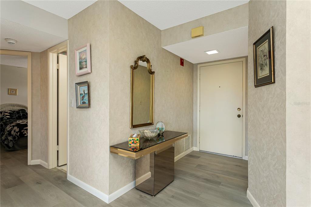 A foyer features a glass-topped console table, a gold-framed mirror, and light wood-look flooring — 3640 IRONWOOD CIRCLE UNIT 503N, BRADENTON, FL