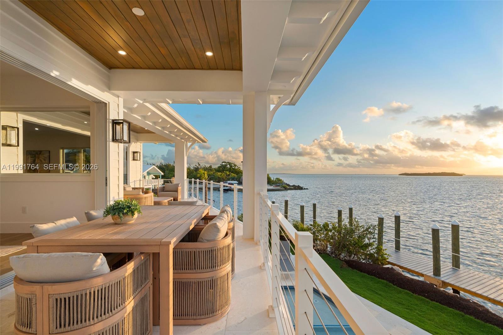 A covered outdoor patio features a wooden dining set overlooking a waterfront dock at sunset — 1002 Snapper Ln, Key Largo FL 33037, KEY LARGO, FL