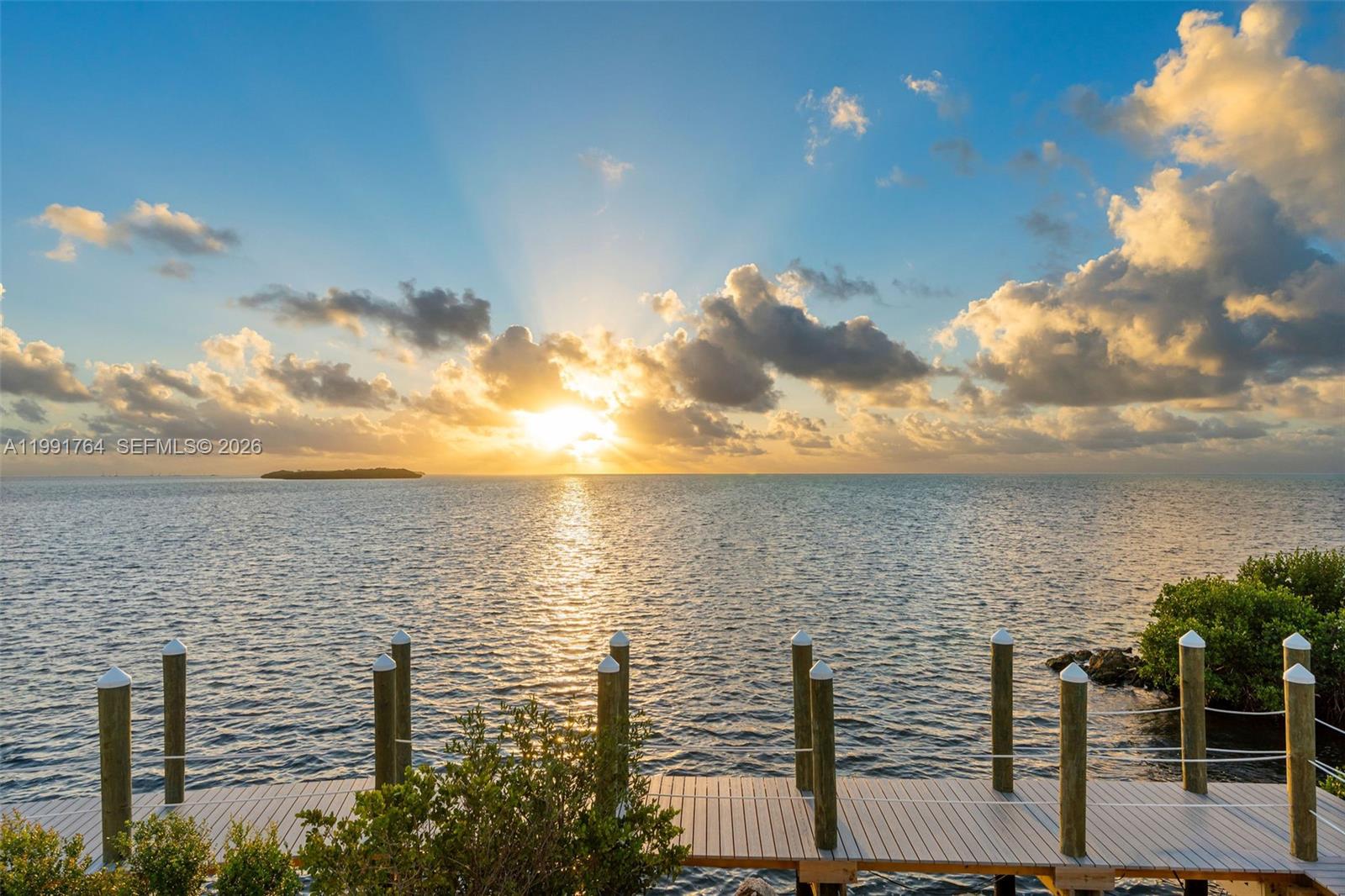 A wooden dock extends into the ocean under a bright sunrise with scattered clouds — 1002 Snapper Ln, Key Largo FL 33037, KEY LARGO, FL