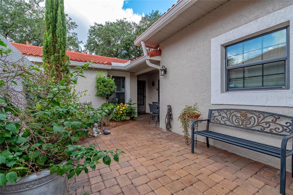 A paved patio area features a metal bench, potted plants, and a house entrance — 7720 CHAPELHILL DRIVE, ORLANDO, FL