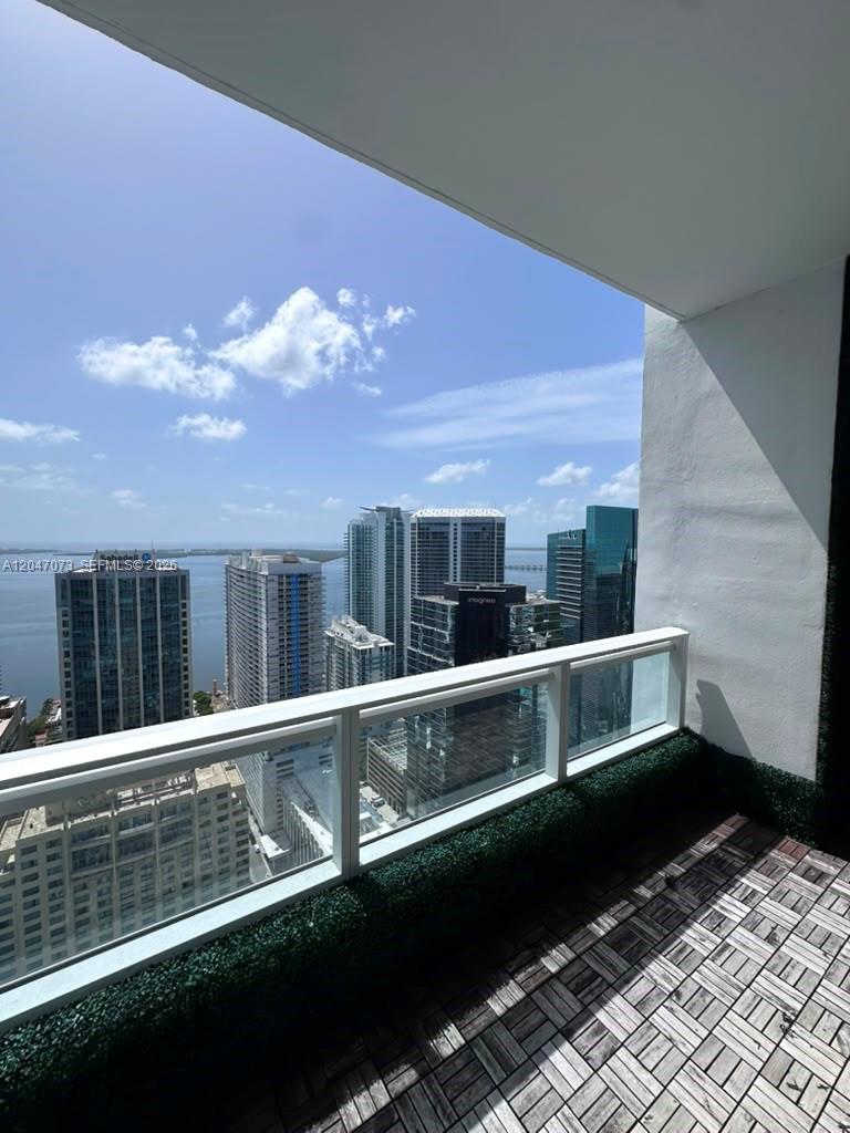 A high-rise balcony with wood-look flooring overlooks a city skyline and a body of water — MIAMI, FL