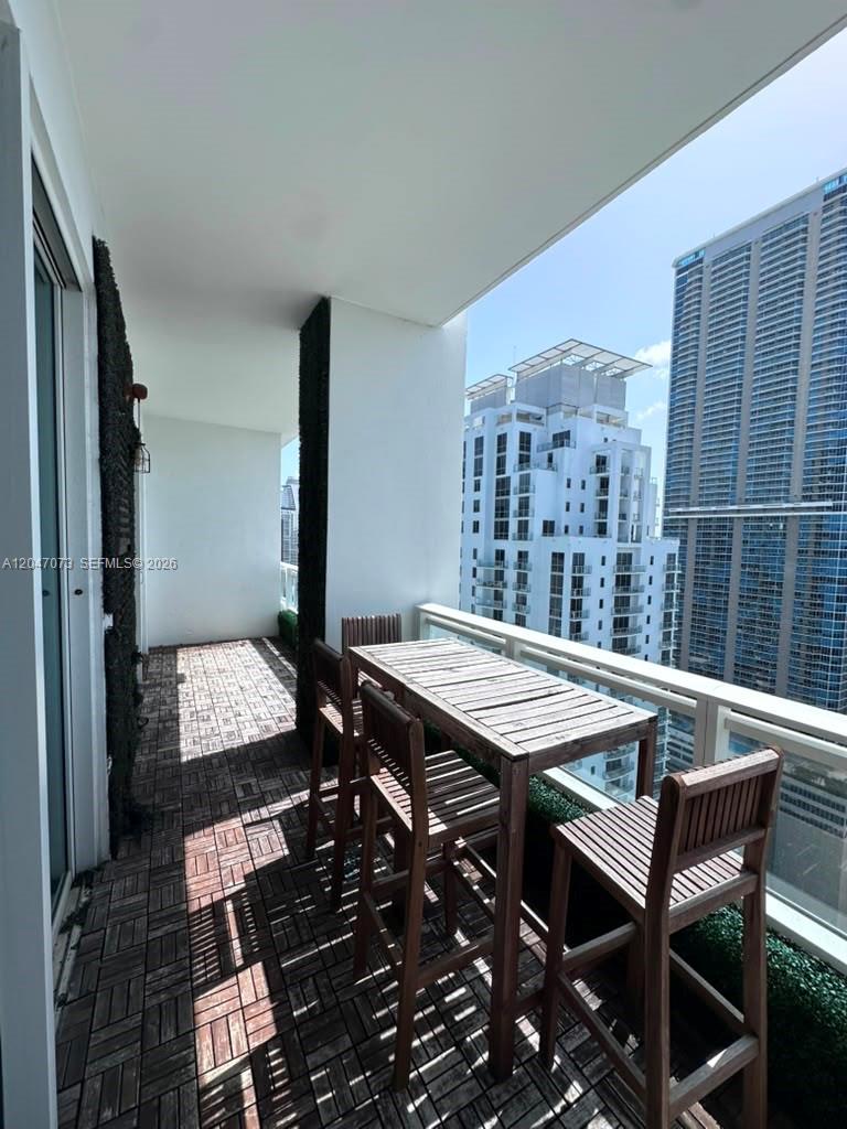 A balcony features wood-look tile flooring, a high-top table with chairs, and city skyline views — MIAMI, FL