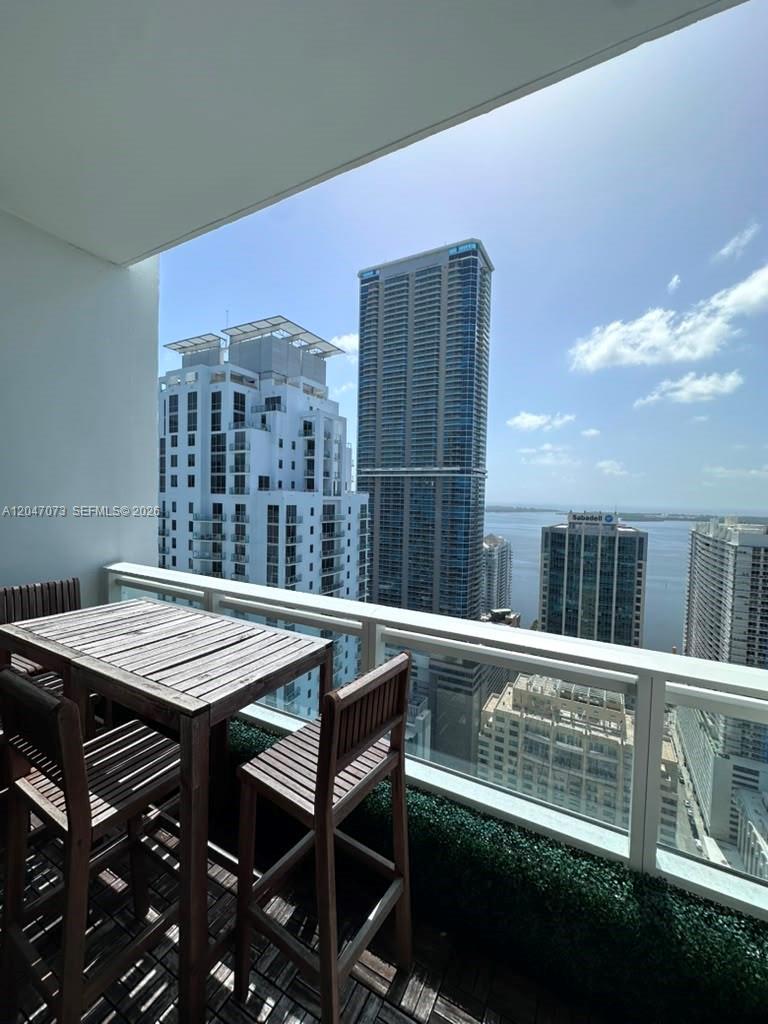A balcony with a wooden table and chairs overlooks a city skyline and water — MIAMI, FL
