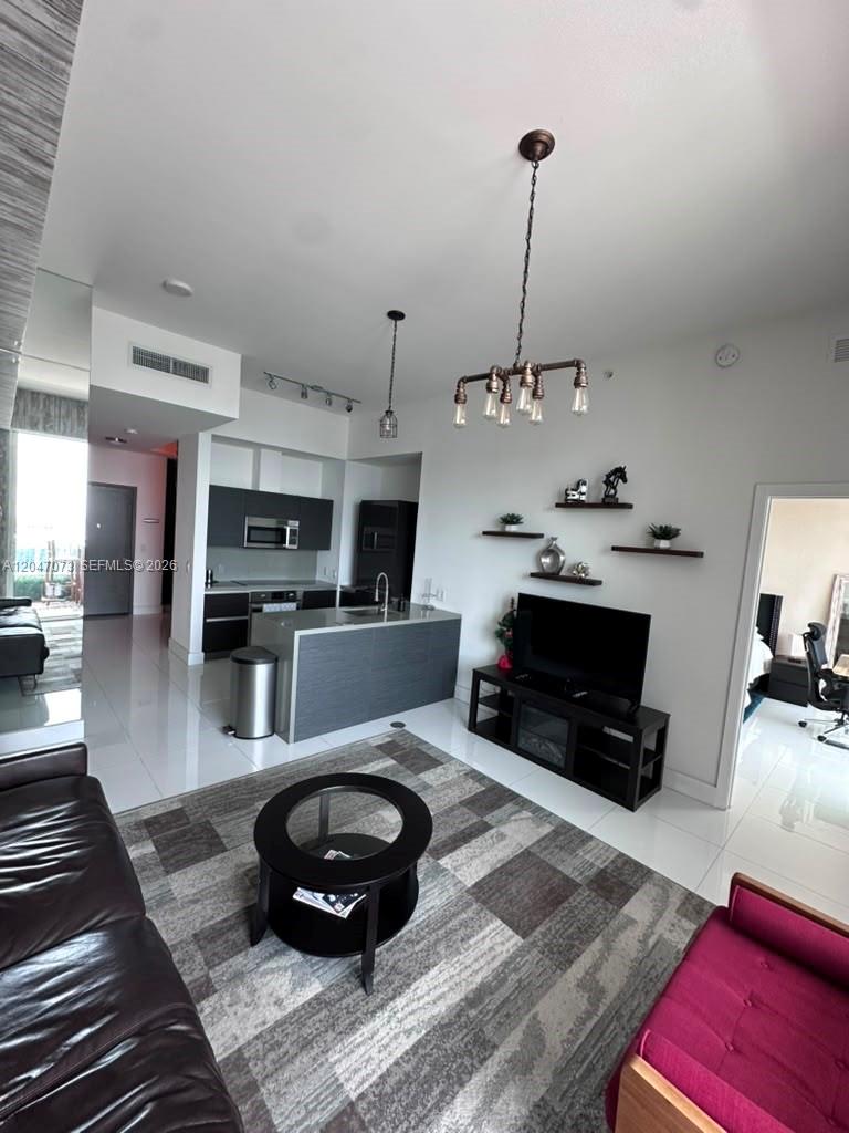 A modern living room and kitchen area with dark cabinetry, tile flooring, and a chandelier — MIAMI, FL