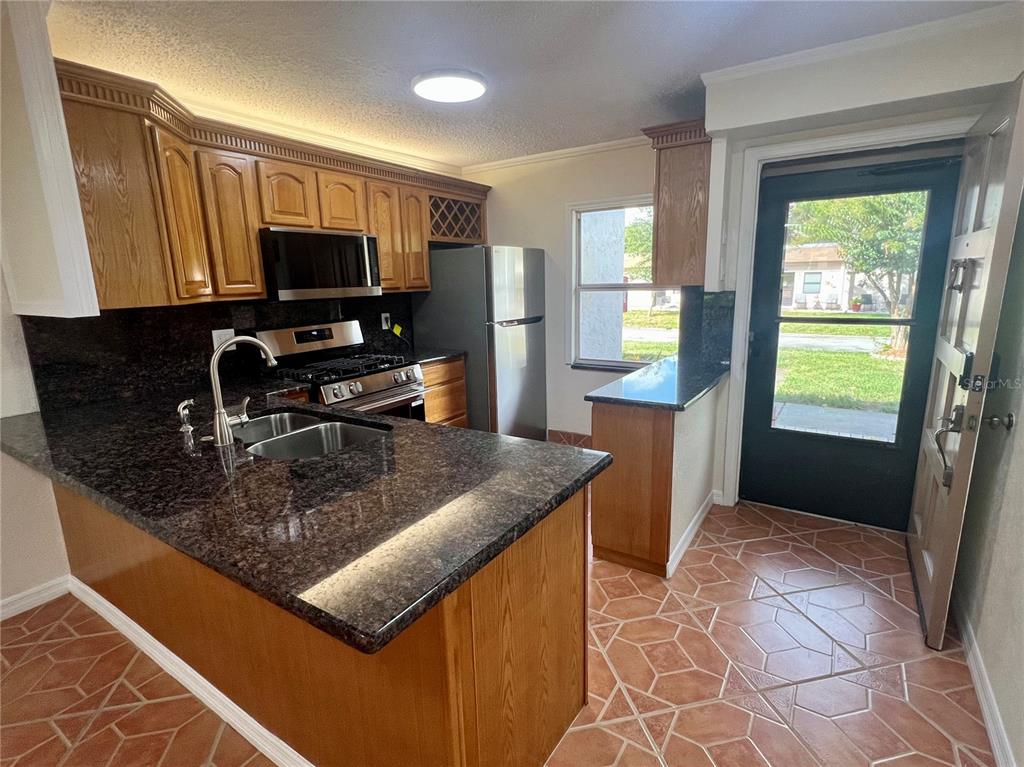 A kitchen features wood cabinets, dark granite countertops, stainless steel appliances, and tiled flooring — 1510 FLINT DRIVE W UNIT 10-F, CLEARWATER, FL