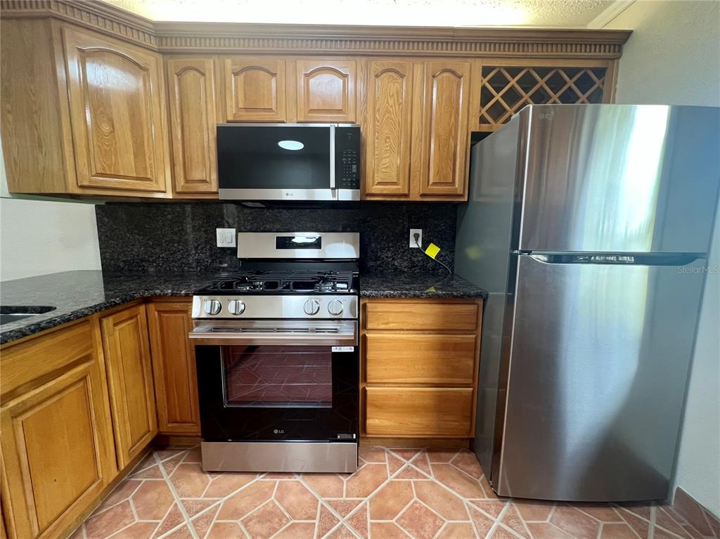 A kitchen features wood cabinets, stainless steel appliances, dark granite countertops, and tiled flooring — 1510 FLINT DRIVE W UNIT 10-F, CLEARWATER, FL