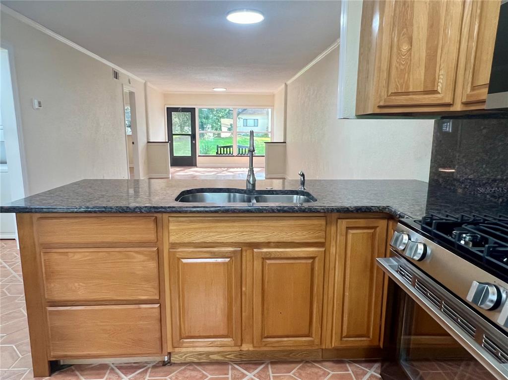 A kitchen island with a double sink and granite countertop faces a living area — 1510 FLINT DRIVE W UNIT 10-F, CLEARWATER, FL