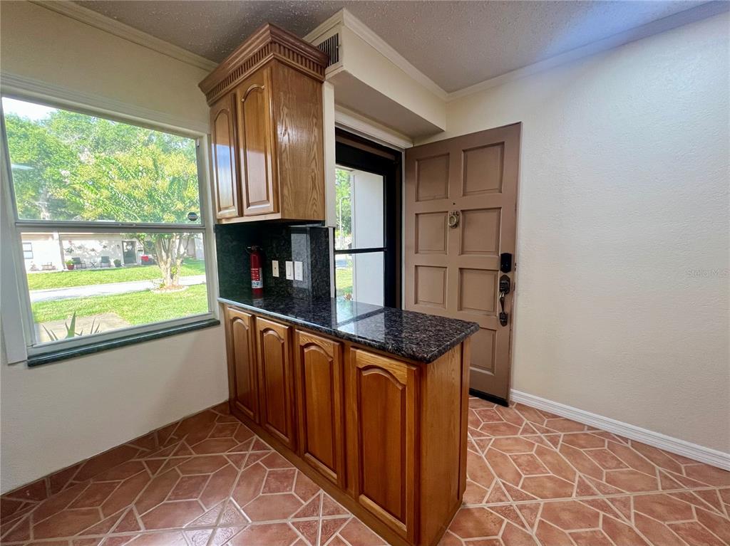 A kitchen area features wood cabinets, dark granite countertops, and tiled flooring near an entrance — 1510 FLINT DRIVE W UNIT 10-F, CLEARWATER, FL