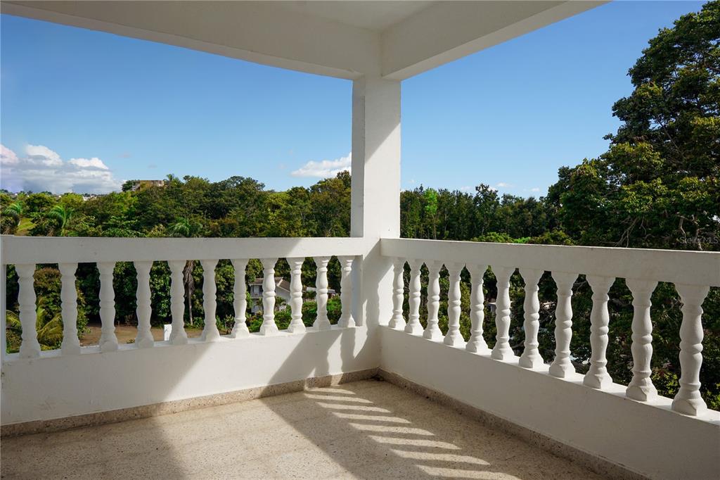 A balcony with white balustrades overlooks a lush green landscape under a clear blue sky — Km 0.1 CARR 412 INT, RINCON, PR