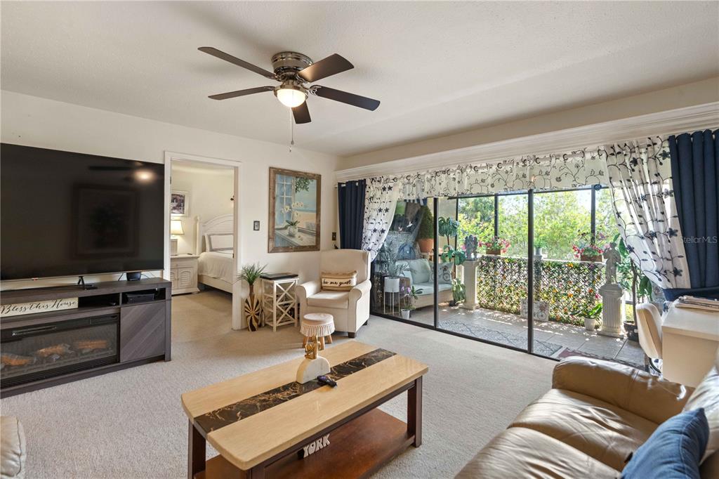A living room features a television, coffee table, beige armchair, and sliding glass doors — 7623 RADCLIFFE CIRCLE UNIT 211A, PORT RICHEY, FL
