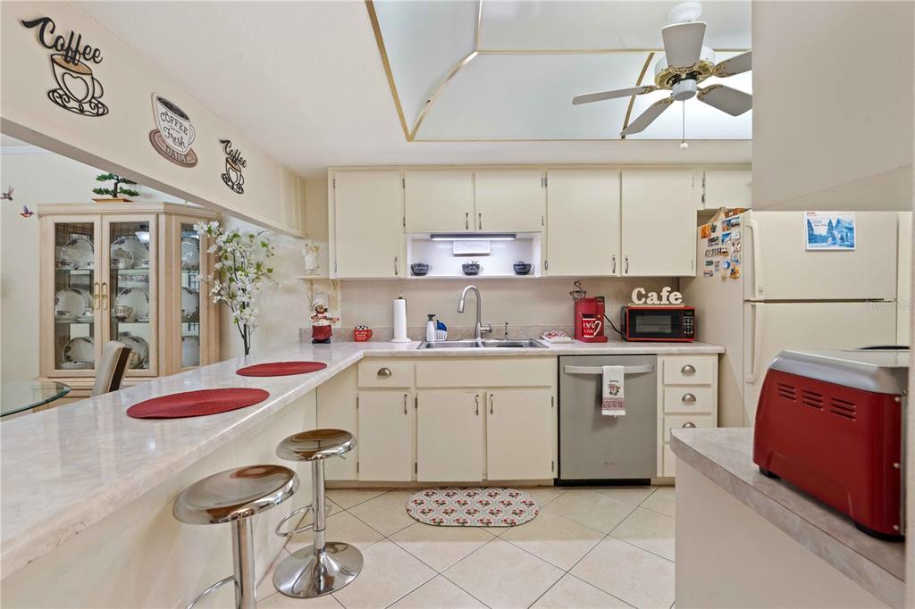 A kitchen features cream cabinets, a breakfast bar with stools, and a ceiling fan — 7623 RADCLIFFE CIRCLE UNIT 211A, PORT RICHEY, FL