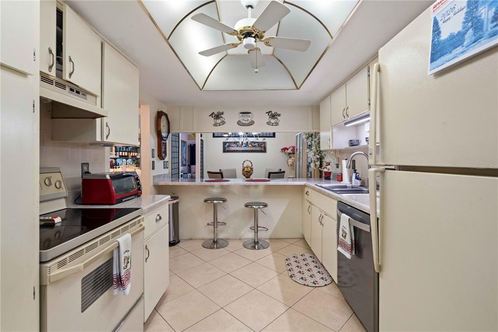 A kitchen features white cabinetry, tile flooring, a breakfast bar, and a ceiling fan — 7623 RADCLIFFE CIRCLE UNIT 211A, PORT RICHEY, FL