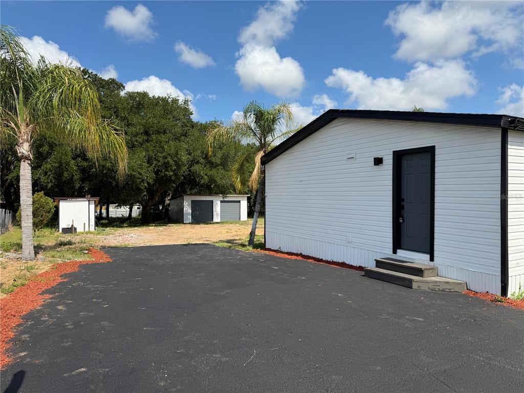 A white mobile home exterior with a black door, asphalt driveway, and detached storage sheds — 3609 FDC GROVE ROAD, DAVENPORT, FL