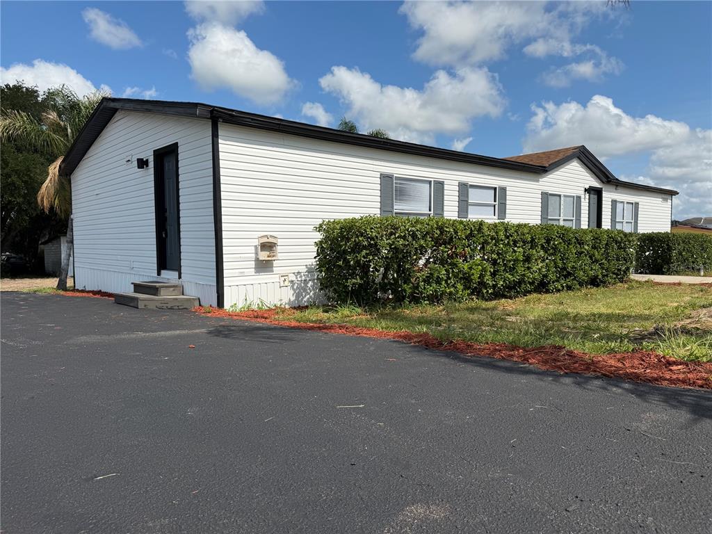 A white mobile home with black trim and a hedge sits beside an asphalt driveway — 3609 FDC GROVE ROAD, DAVENPORT, FL