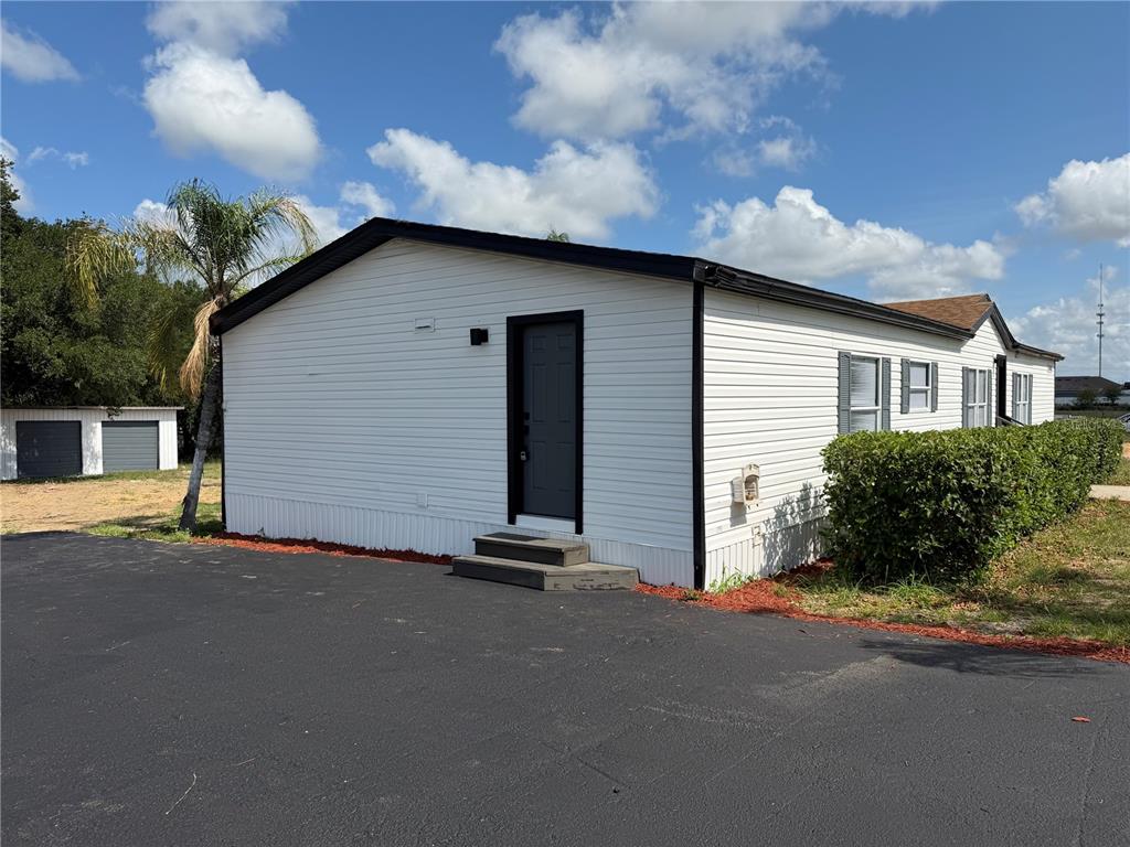 A white mobile home with black trim and a dark door sits next to asphalt — 3609 FDC GROVE ROAD, DAVENPORT, FL