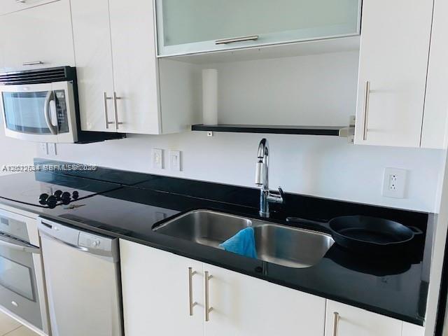 A modern kitchen features white cabinets, black countertops, a stainless steel microwave, and a sink — 60 SW 13th St # 3622, Miami FL 33130, MIAMI, FL