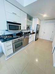 A modern kitchen features white cabinetry, stainless steel appliances, and light-colored tile flooring — 60 SW 13th St # 3622, Miami FL 33130, MIAMI, FL