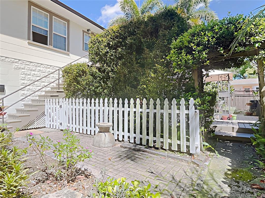 A white picket fence separates a brick patio from a house with exterior stairs — 1601 11 STREET N, ST PETERSBURG, FL