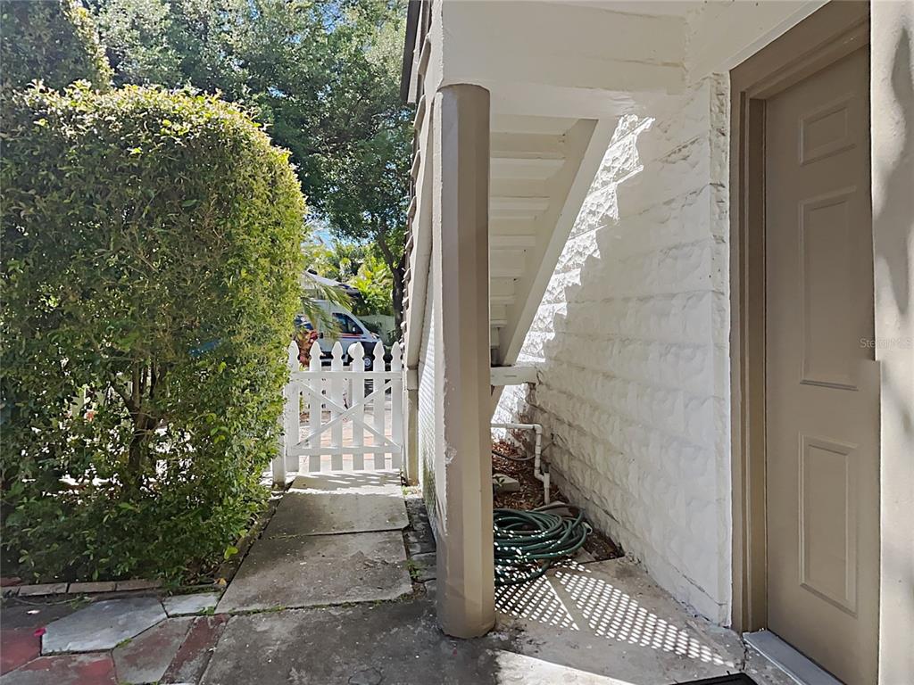 A concrete walkway leads to a white picket gate beside an exterior staircase and door — 1601 11 STREET N, ST PETERSBURG, FL