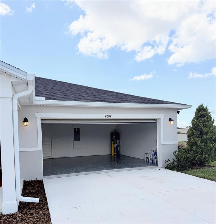 An open garage with a concrete floor, white walls, and two exterior wall sconces — 2602 LOLA LANE, KISSIMMEE, FL