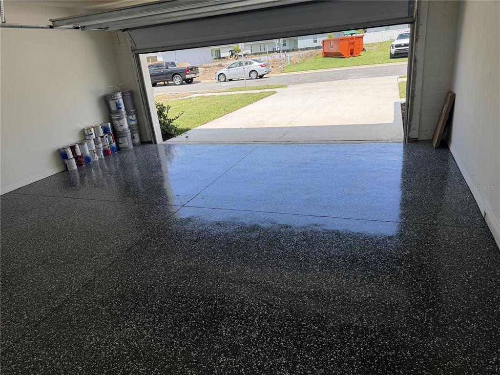 A garage with a glossy, speckled epoxy floor and paint cans stacked in the corner — 2602 LOLA LANE, KISSIMMEE, FL