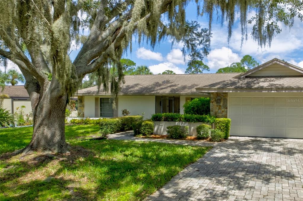 A single-story house with a paved driveway, stone accents, and a large tree with moss — 5115 EVERWOOD RUN, SARASOTA, FL