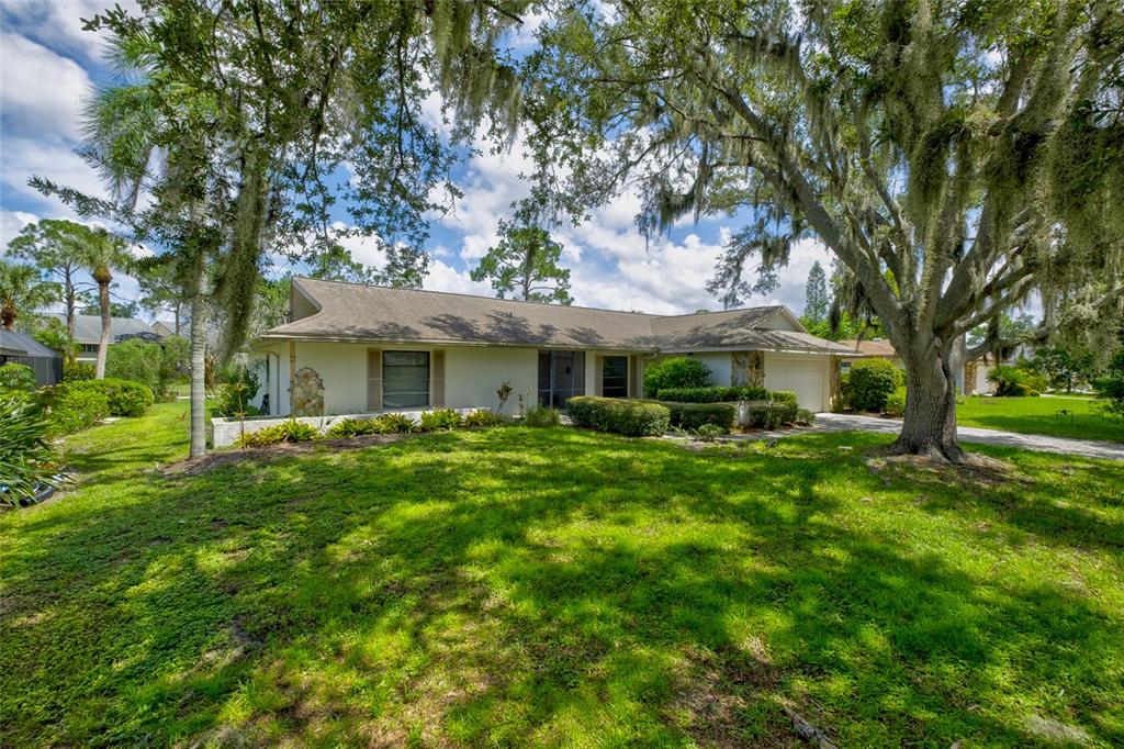 A single-story house with a light-colored exterior, a shingled roof, and large oak trees — 5115 EVERWOOD RUN, SARASOTA, FL