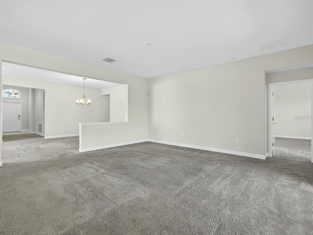 A spacious, carpeted living room features neutral walls and a doorway leading to another room — 466 BRUNSWICK DRIVE, DAVENPORT, FL