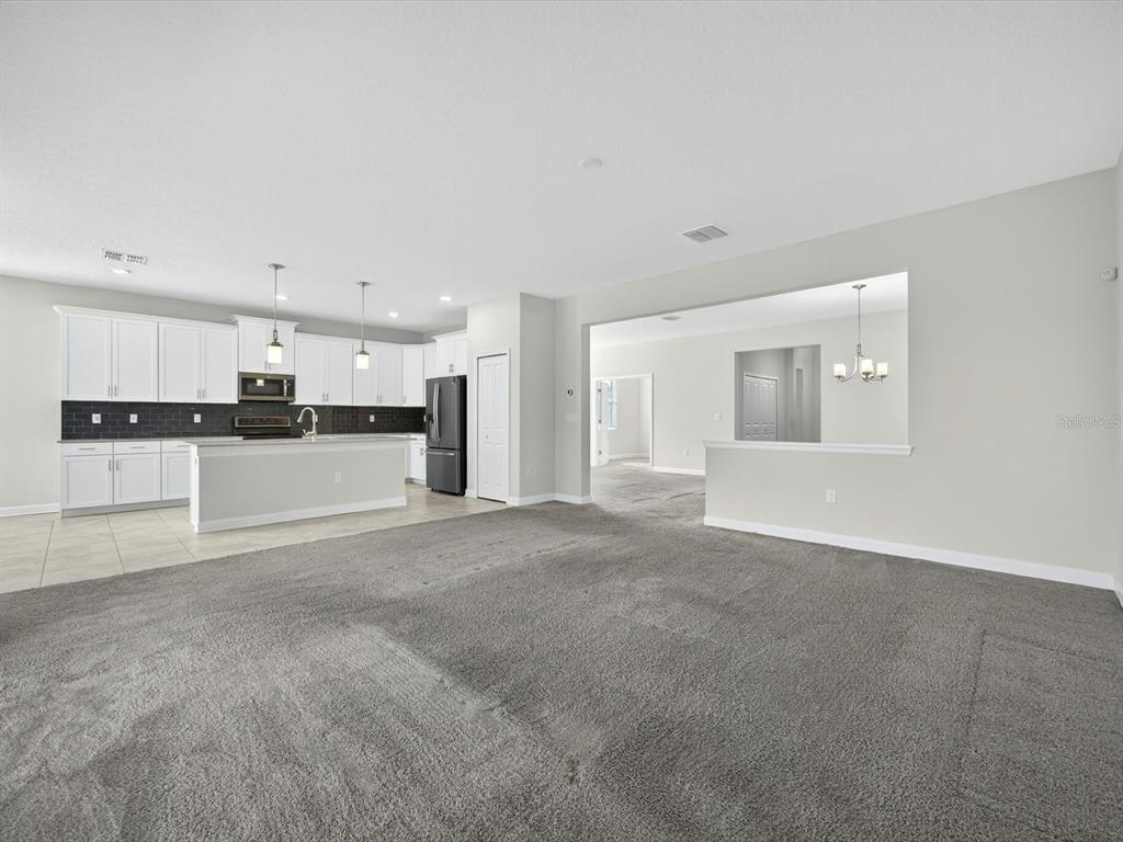 An open-concept living area features gray carpeting, a white kitchen with an island, and neutral walls — 466 BRUNSWICK DRIVE, DAVENPORT, FL