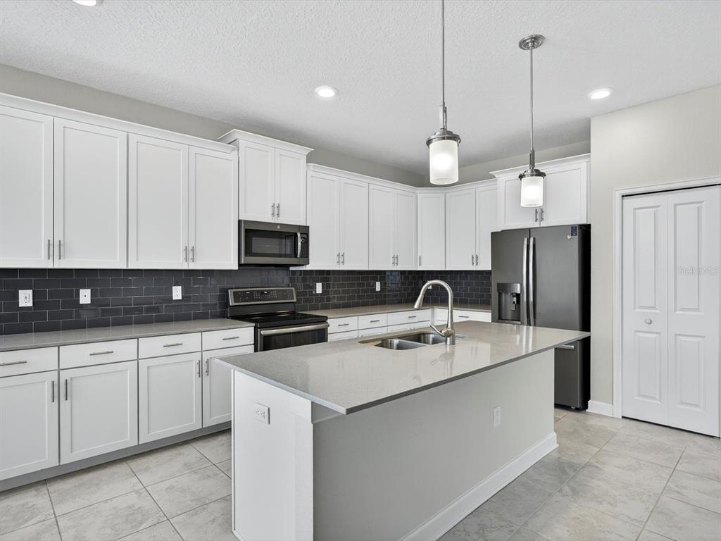 A kitchen features white cabinets, dark tile backsplash, a gray island, and stainless steel appliances — 466 BRUNSWICK DRIVE, DAVENPORT, FL