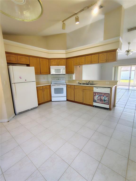 A kitchen with light wood cabinets, white appliances, and tile flooring under a vaulted ceiling — 3248 SAWGRASS CREEK CIRCLE, ST CLOUD, FL