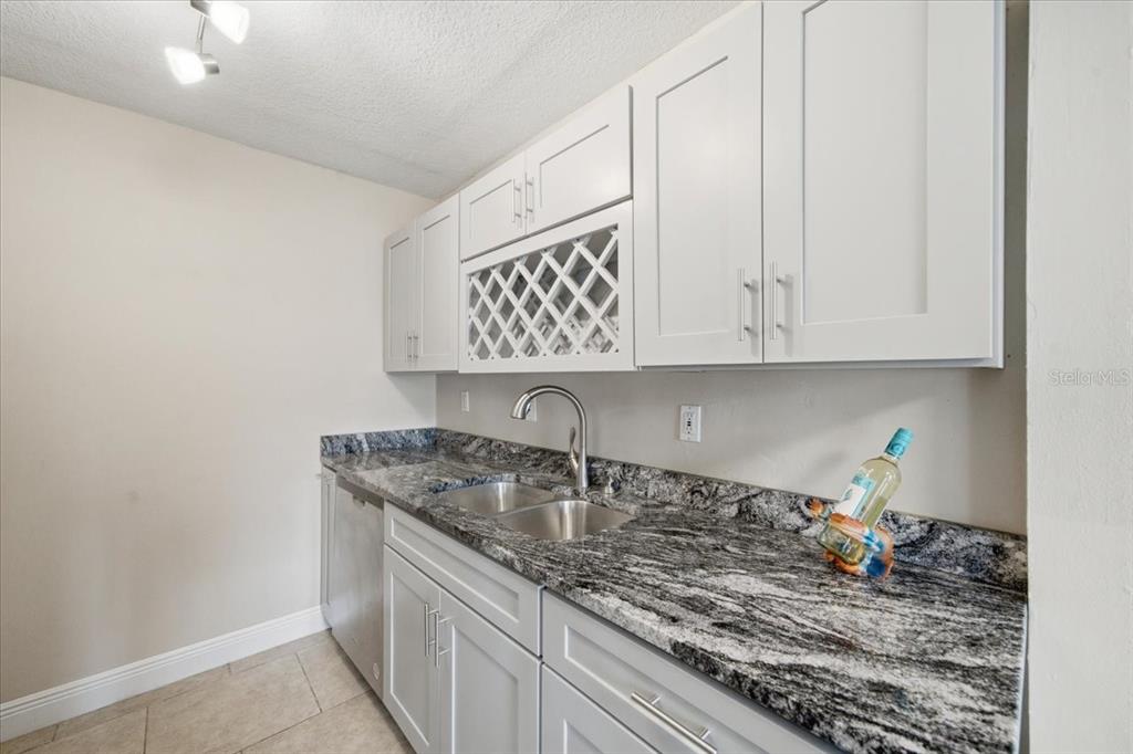 A kitchen features white cabinets, a wine rack, granite countertops, and a stainless steel sink — 4843 COQUINA KEY DRIVE SE UNIT A, ST PETERSBURG, FL