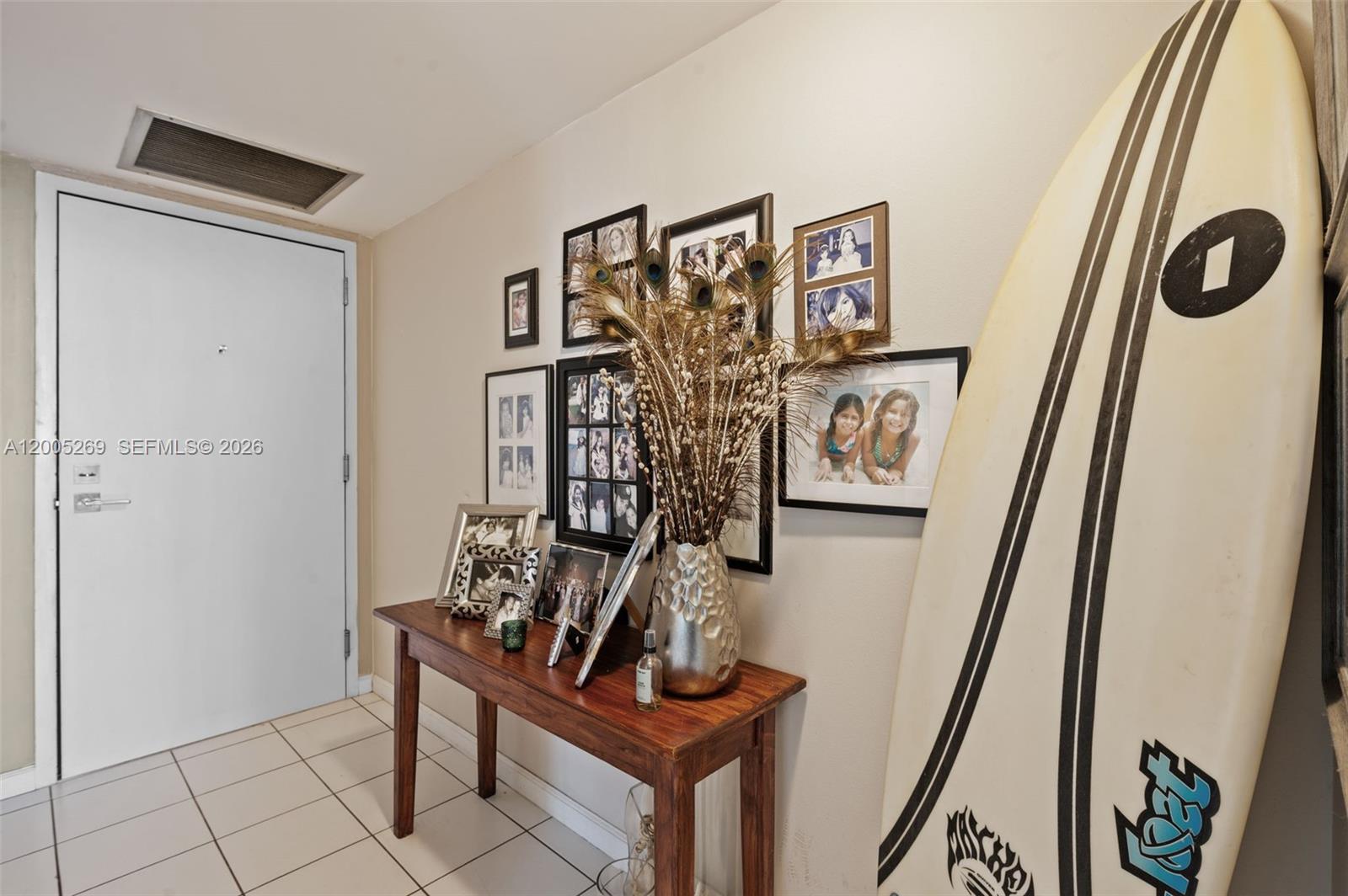 A wooden console table sits against a wall decorated with framed photos and a surfboard — 2555 Collins Ave # 1002, Miami Beach FL 33140, MIAMI BEACH, FL