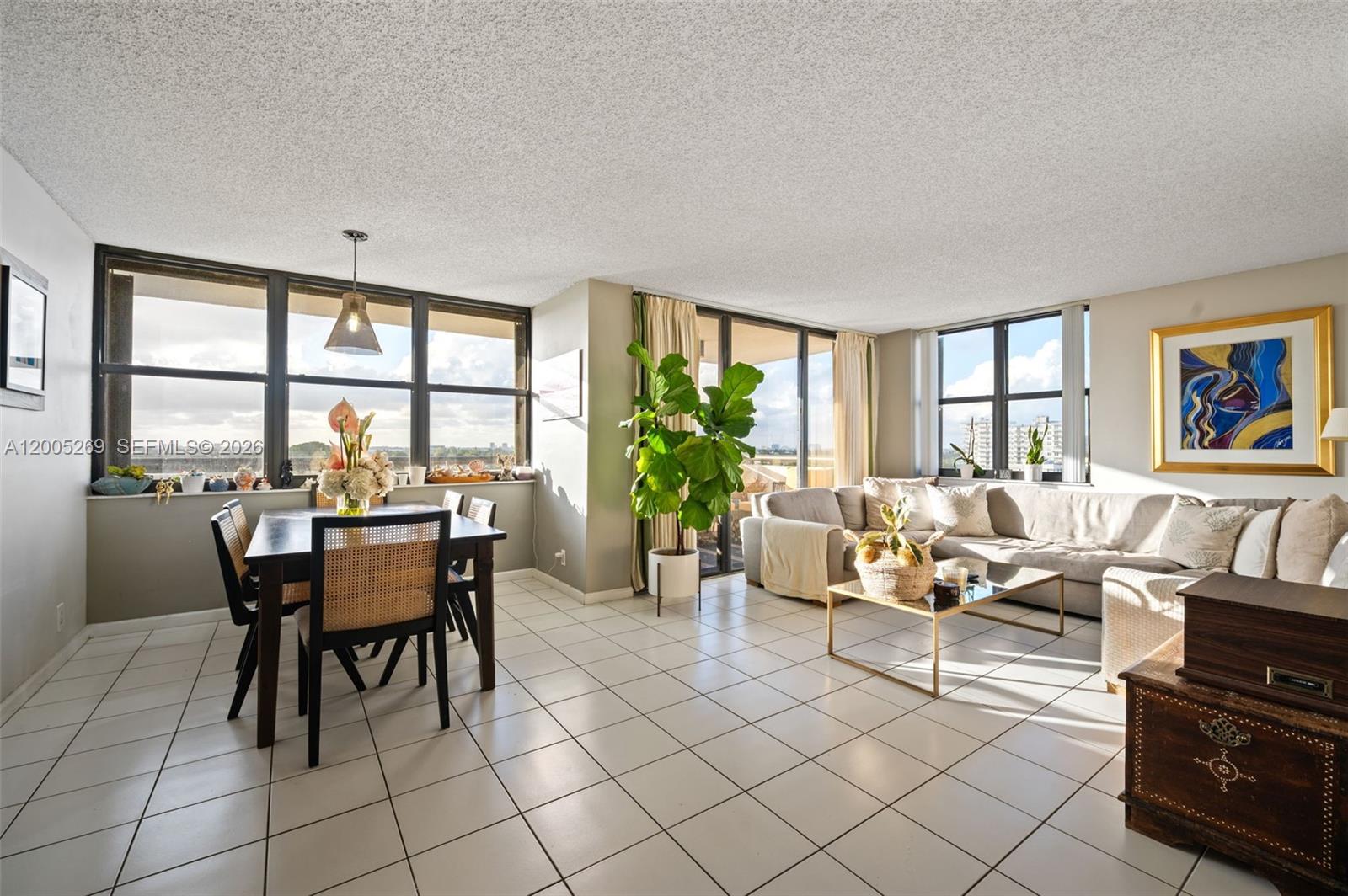 A bright living and dining area features white tile floors, large windows, and a sectional — 2555 Collins Ave # 1002, Miami Beach FL 33140, MIAMI BEACH, FL