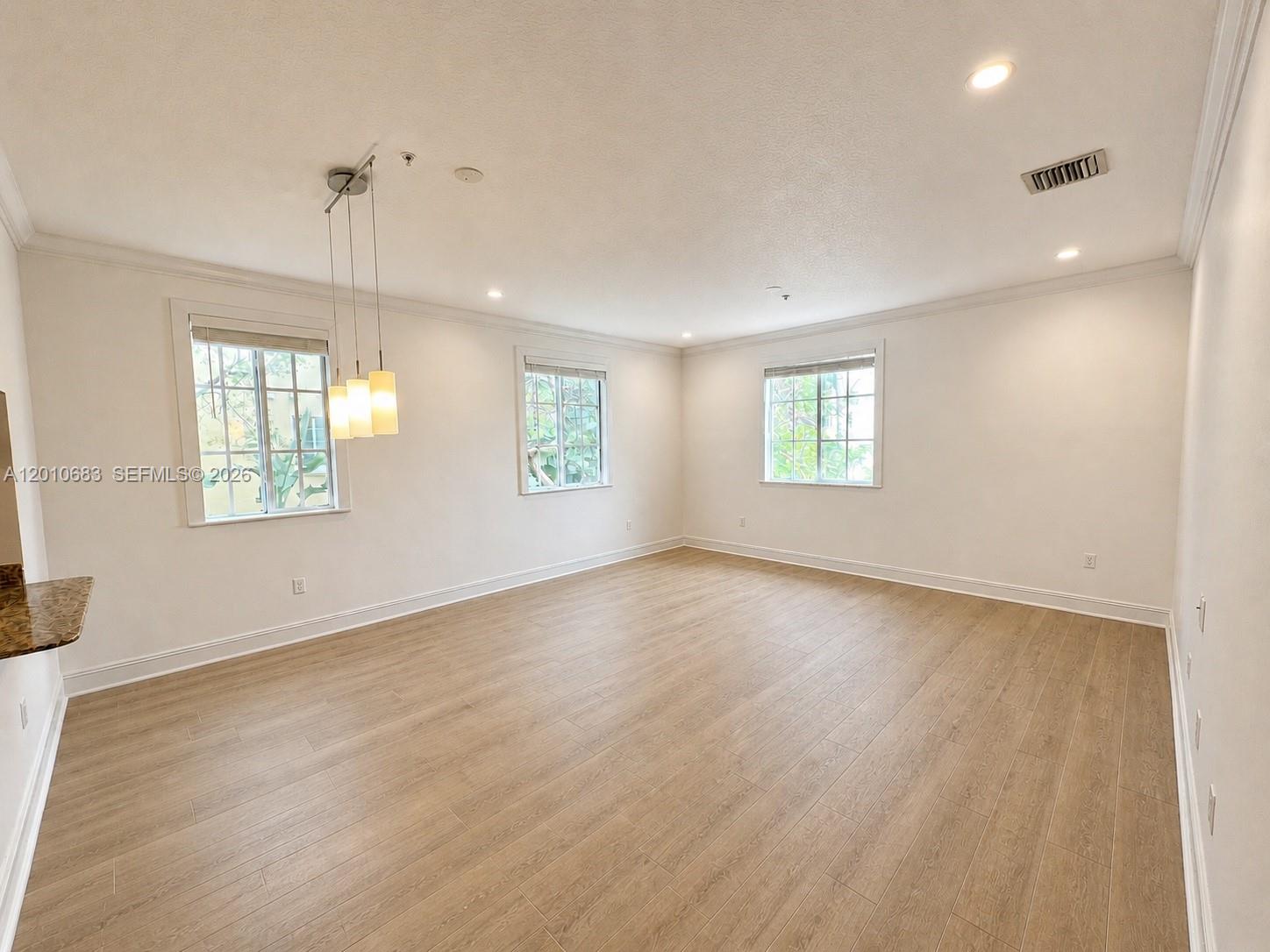 An empty room features light wood-look flooring, white walls, three windows, and a hanging light fixture — 115 Mendoza Ave # 202, Coral Gables FL 33134, CORAL GABLES, FL