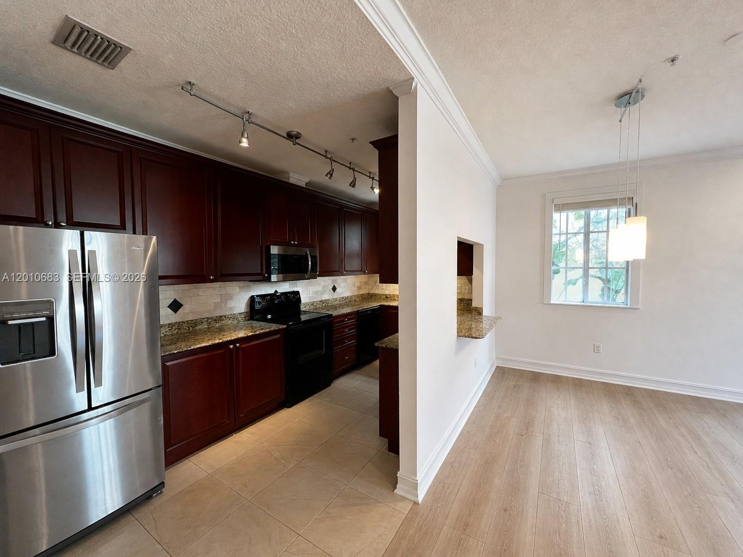 A kitchen with dark wood cabinets and granite countertops opens into a dining area — 115 Mendoza Ave # 202, Coral Gables FL 33134, CORAL GABLES, FL