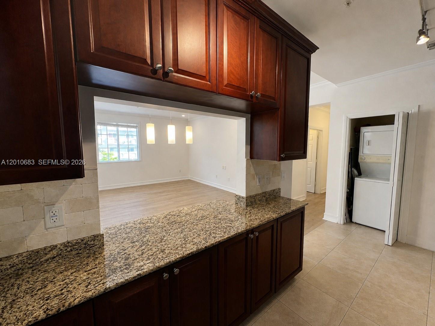 A kitchen with dark wood cabinets and granite countertops overlooks an adjacent living area — 115 Mendoza Ave # 202, Coral Gables FL 33134, CORAL GABLES, FL