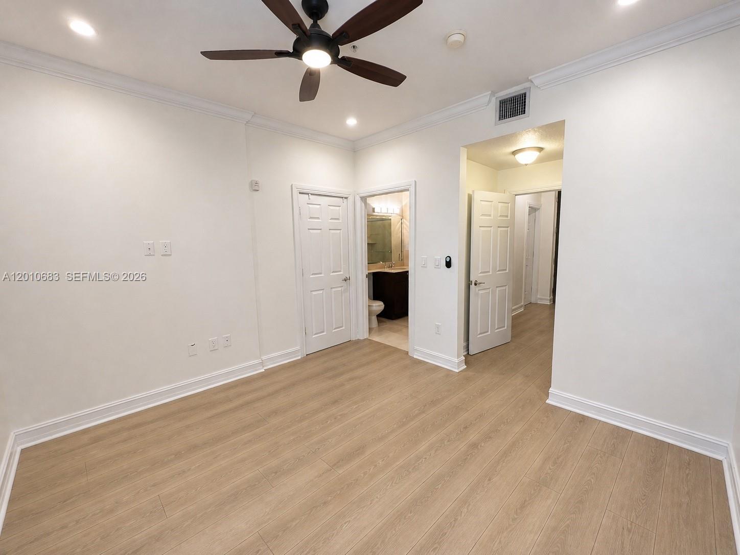 An empty bedroom features light wood-look flooring, white walls, a ceiling fan, and two doorways — 115 Mendoza Ave # 202, Coral Gables FL 33134, CORAL GABLES, FL